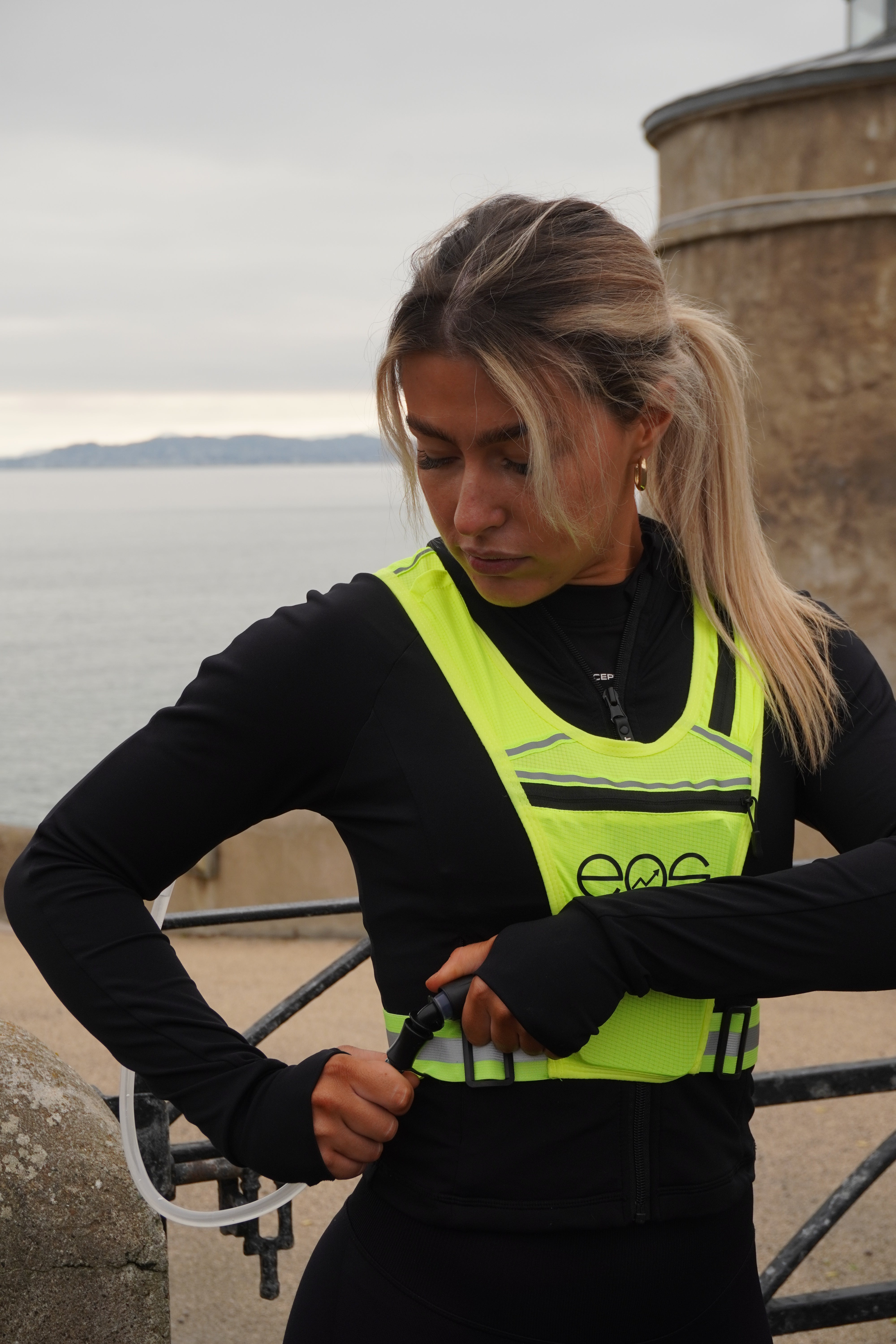 Eos Elite brand ambassador Anna Lalor adjusts the straps of her yellow IlluminLight running vest whilst outside