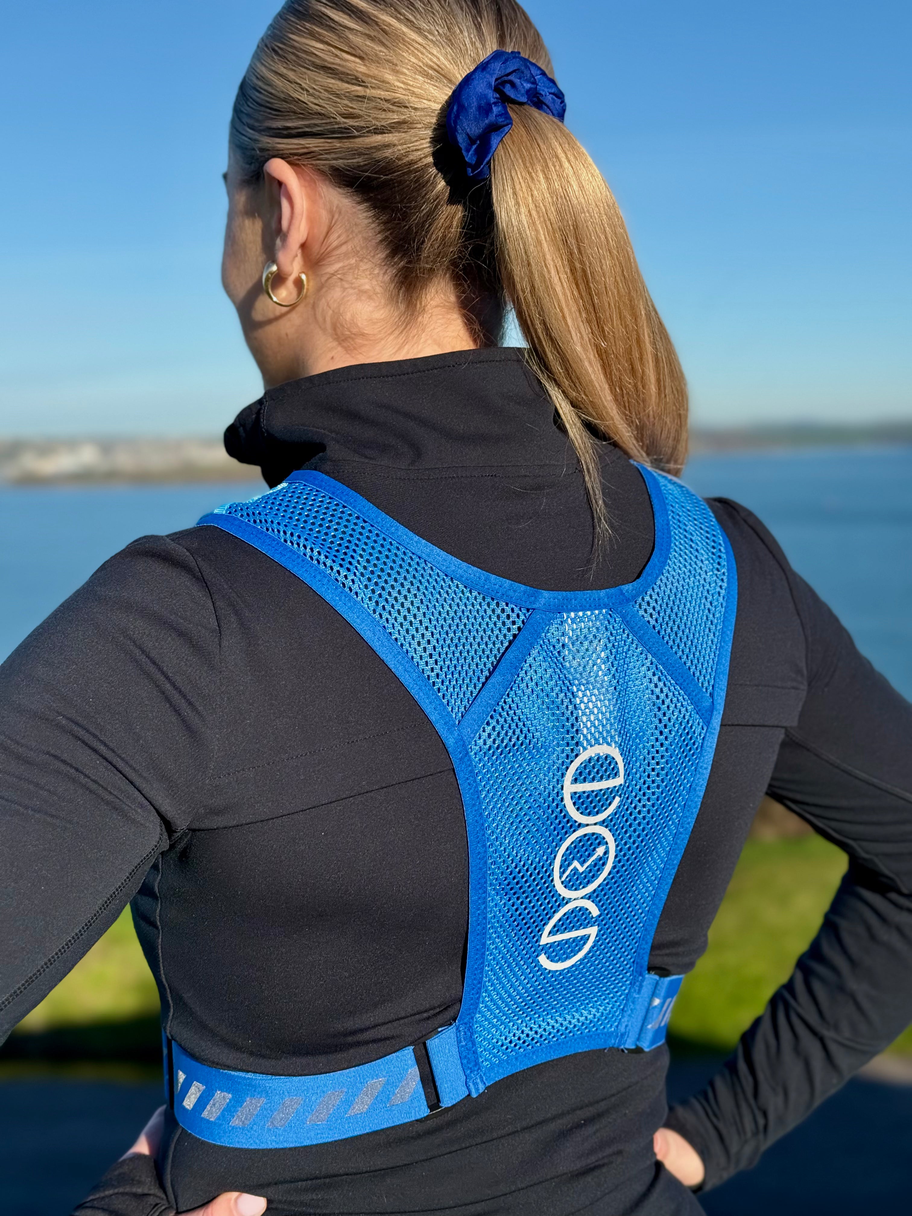 Eos Elite brand ambassador Erica Deasy is photographed wearing the blue Eos Elite RainGuard running best. From the back the water bladder pocket and adjustable straps are clearly visible