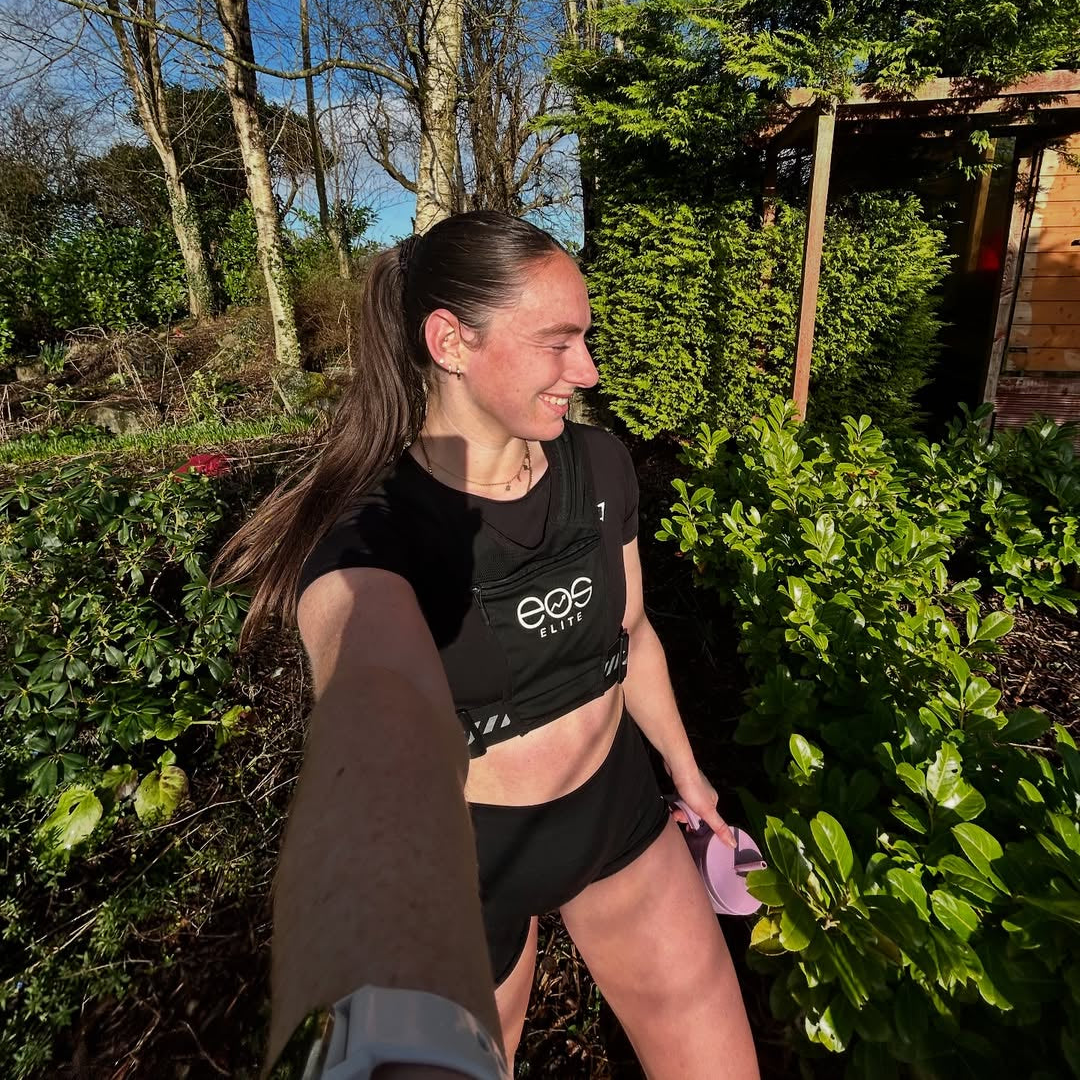 Eos Elite brand ambassador Sarah Cuddy takes a selfie whilst outdoors in the sunshine wearing a black Eos Elite running best and carrying a water bottle